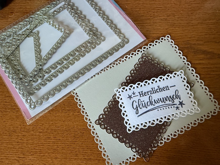 Kartenkunst: Eine Kombination aus rechteckigen Stanzschablonen mit Zierkante, ausgeschnittenen Formen aus verschiedenen Papiersorten und dem Schriftzug "Herzlichen Glückwunsch"
