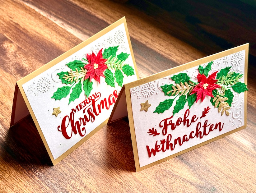 Zwei luxuriöse 3D-Weihnachtskarten im Querformat. Ein Gesteck aus einem roten Weihnachtsstern, Stechpalmen und goldenen Farnen liegt auf einem weißen Hintergrund mit Schneeflocken-Struktur. Erhältlich mit dem Schriftzug 'Frohe Weihnachten' oder 'Merry Christmas