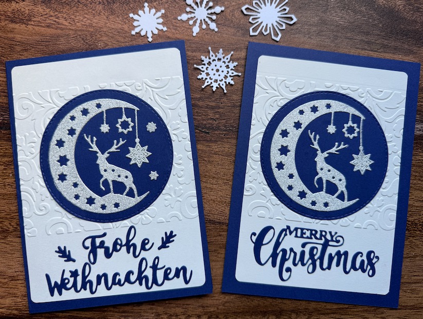 Zwei elegante 3D-Weihnachtskarten mit geprägtem Hintergrund in Dunkelblau und Weiß. Das Hauptmotiv ist ein Medaillon mit einem Rentier in einem silber glitzernden Halbmond. Die Karte ist mit dem Schriftzug 'Frohe Weihnachten' oder 'Merry Christmas' erhältlich